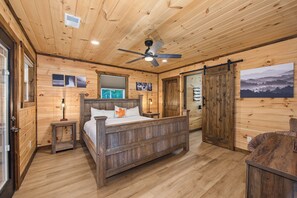 Une chambre dans une cabane en bois, avec un lit, un ventilateur de plafond et une grande fenêtre.