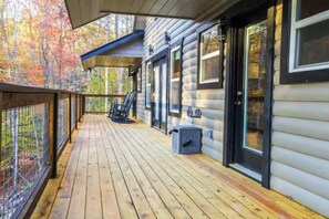 Une terrasse en bois avec une rambarde, un espace abrité et une vue sur une forêt.