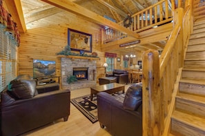 A log cabin interior with a stone fireplace, leather sofas, a television, and a wooden staircase. - Welcome to LeConte Lookout, your perfect Sevierville escape designed for family (Sevierville)