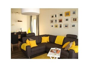 Uma sala de estar moderna com sofá seccional, área de jantar e parede com quadros emoldurados.