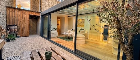 A modern house with a glass-enclosed patio, wooden furniture, and a potted plant.
