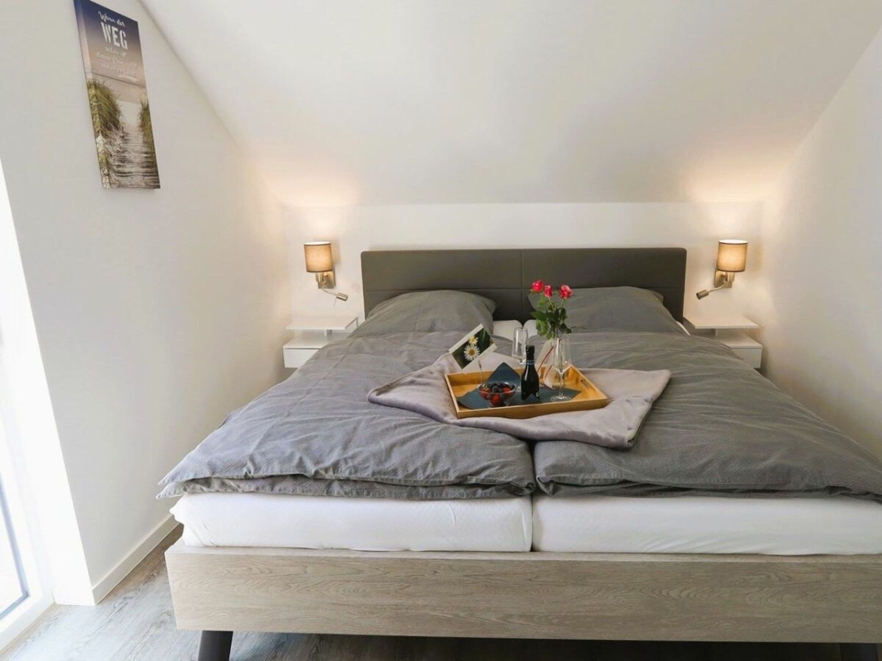 A neatly made bed with a tray of breakfast items, two bedside lamps, and a framed picture on the wall.