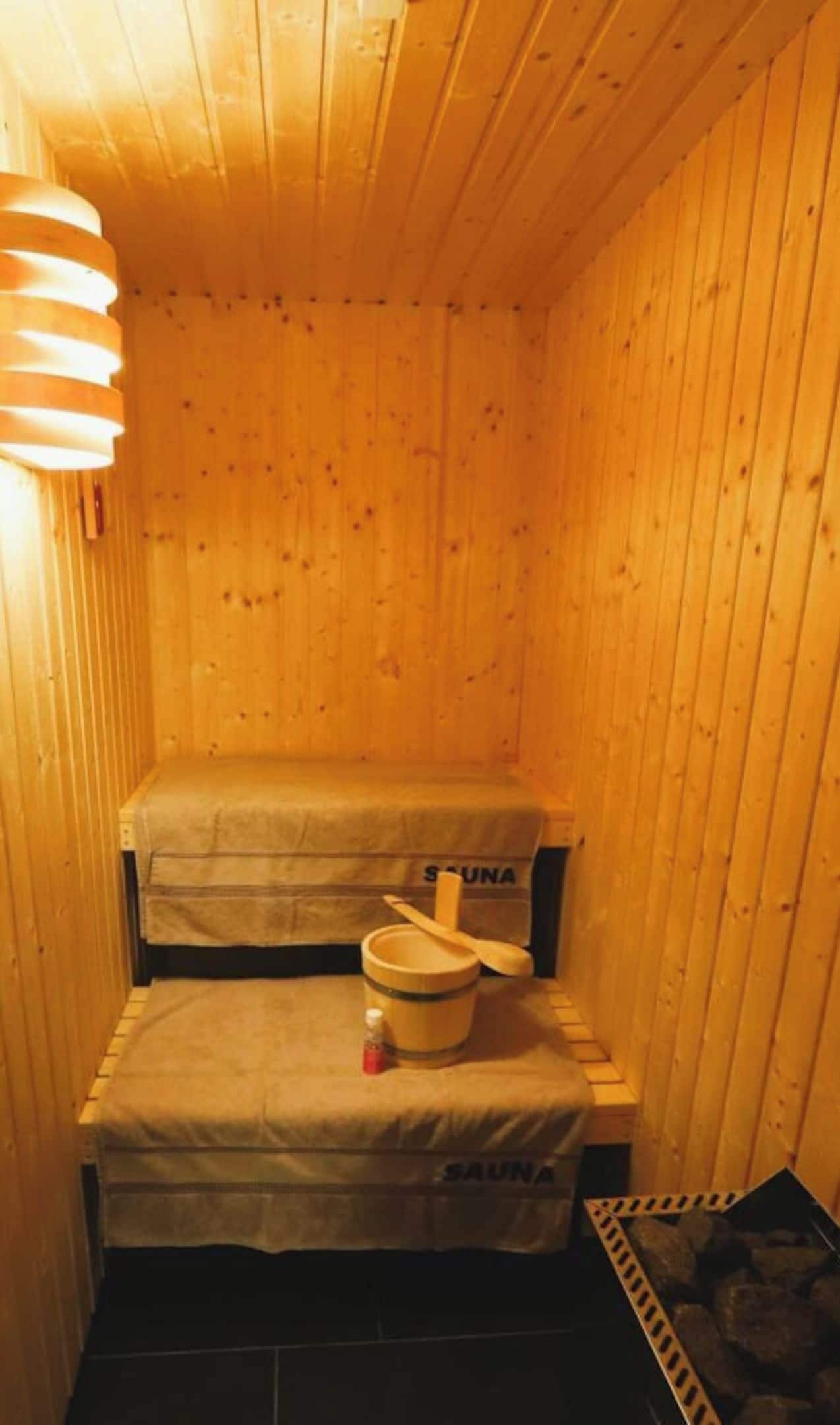 A sauna room with wooden walls, a bench, a wooden bucket, and a sauna mat.