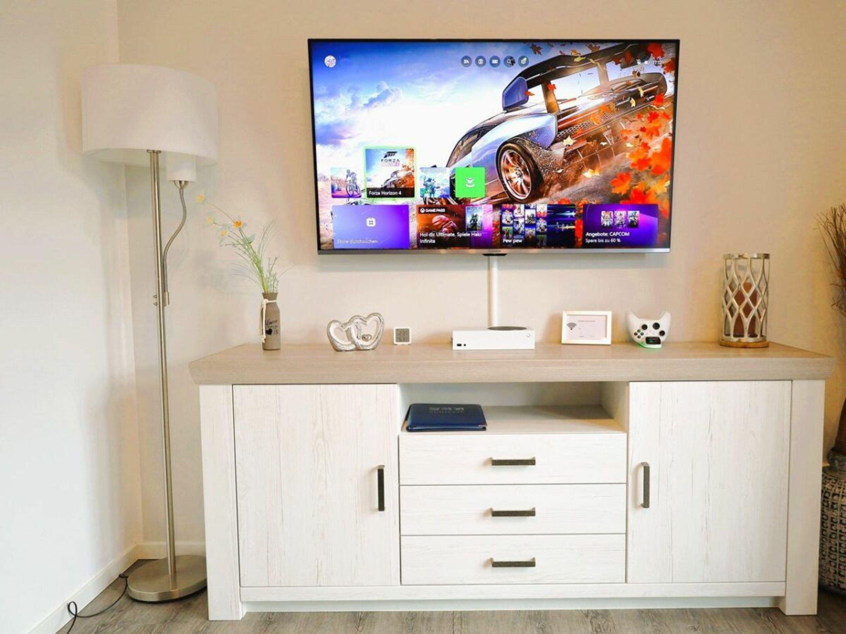 Una TV a schermo piatto montata a parete sopra un mobile in legno con cassetti e un ripiano.