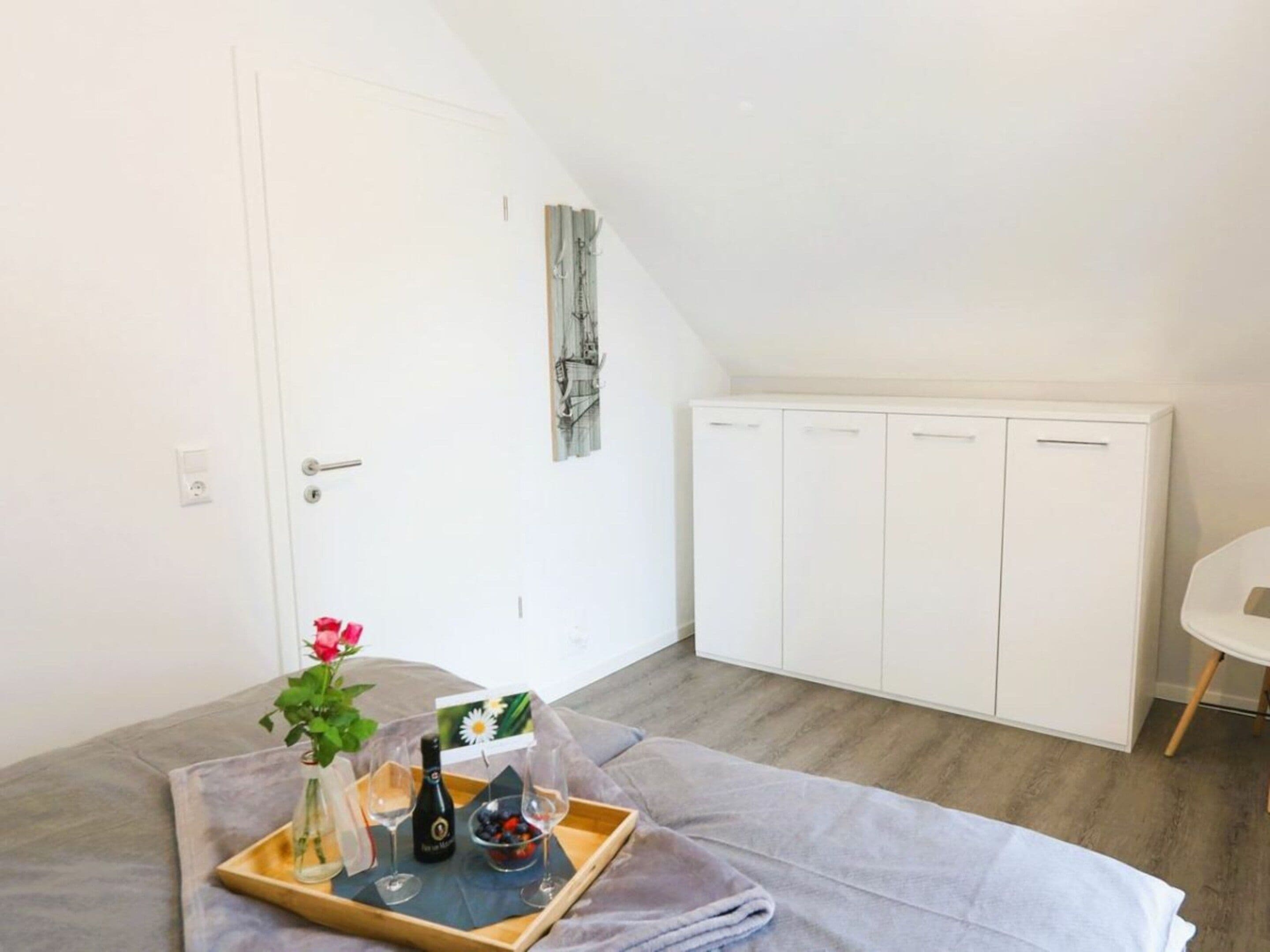 A room with a bed, a bedside table with a tray of breakfast items, a white wardrobe, and a small round table.