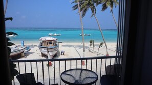 A beach view from a balcony with a table and chairs, a boat named 'FALCON' on the sand, and palm trees.