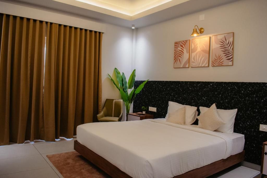 A hotel room with a large bed, a nightstand, a chair, a plant, and artwork on the wall.