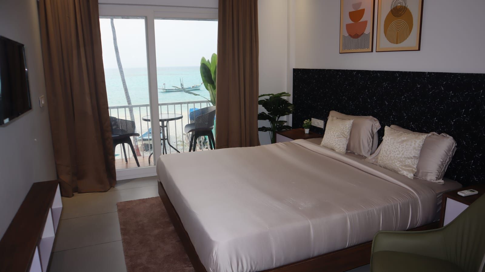 Une chambre d’hôtel avec un grand lit, une vue sur la mer, un balcon avec des chaises et un téléviseur fixé au mur.