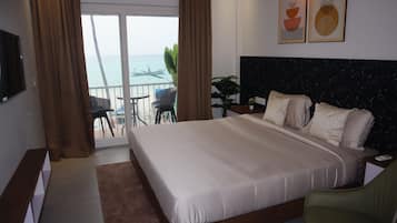 Une chambre d’hôtel avec un grand lit, une vue sur la mer, un balcon avec des chaises et un téléviseur fixé au mur.