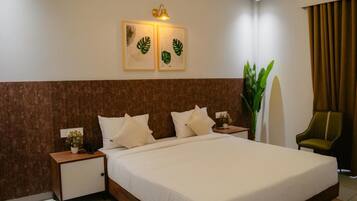 A hotel room with a large bed, two bedside tables, a nightstand, a potted plant, a chair, and artwork on the wall.