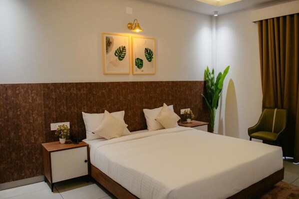 A hotel room with a large bed, two bedside tables, a nightstand, a potted plant, a chair, and artwork on the wall.