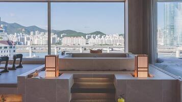 Ein modernes Hotelzimmer mit großem Fenster und Blick auf die Stadt, einer kleinen Sitzecke und einer Treppe, die in eine obere Ebene führt.