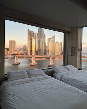 Ein Hotelzimmer mit zwei Betten und einem großen Fenster mit Blick auf die Stadt.