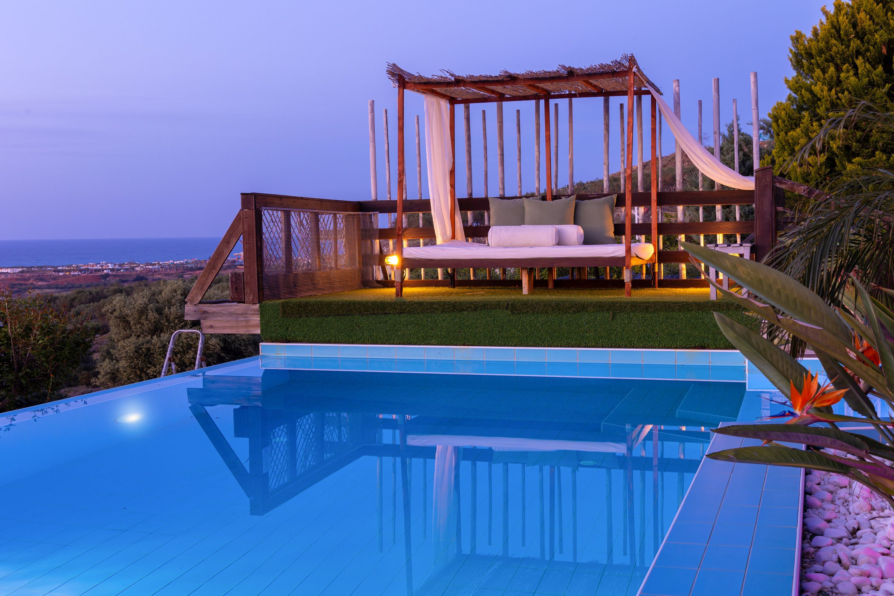 Une piscine avec une terrasse en bois et un lit avec des oreillers.