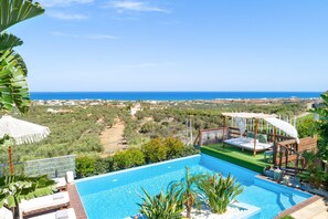 A pool with a view of the sea and a wooden deck with a bed. - Villa Konstantinos in Heraklion (Heraklion)