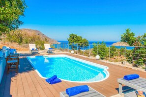 Ein Swimmingpool mit Liegestühlen und Blick aufs Meer.