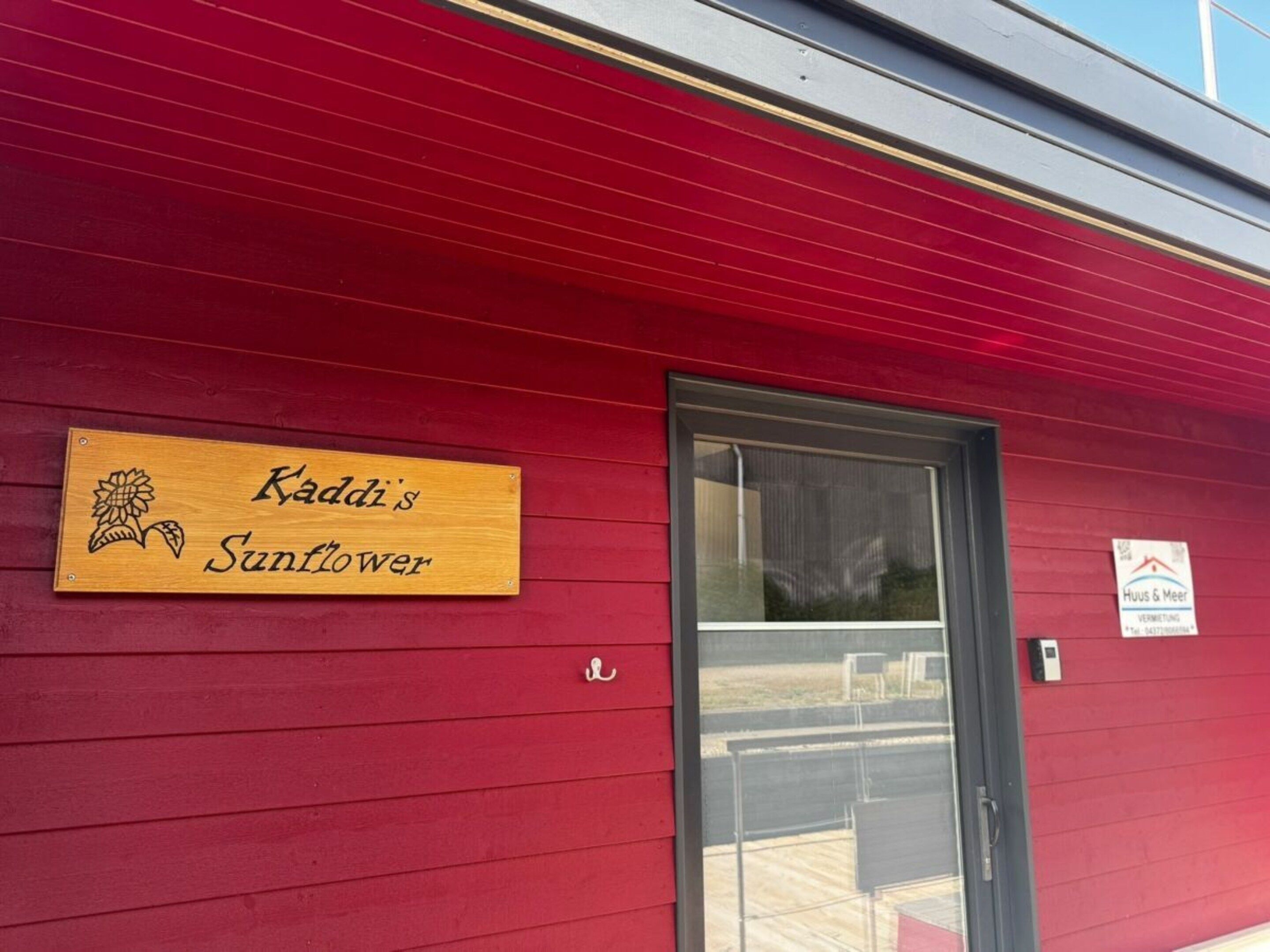 En rød bygning med et træskilt der siger 'Kaddi's Sunflower' og en dør.
