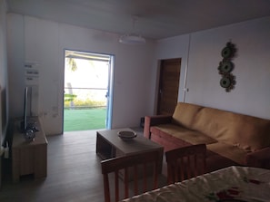 A room with a sofa, a table, a chair, a television, and a door leading to an outdoor area. - A Saint Leu Maison créole bien équipée avec jacuzzi et vue imprenable sur la mer (Saint-Leu)