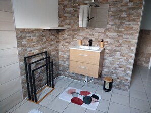 Une salle de bain avec un mur en pierre, un meuble en bois avec des tiroirs, un miroir et un espace douche.