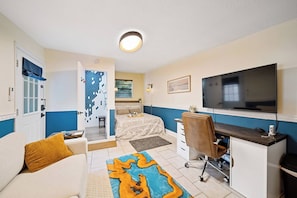 Een kleine hotelkamer met een bed, een bureau, een stoel, een televisie en een badkamer met douche en toilet.