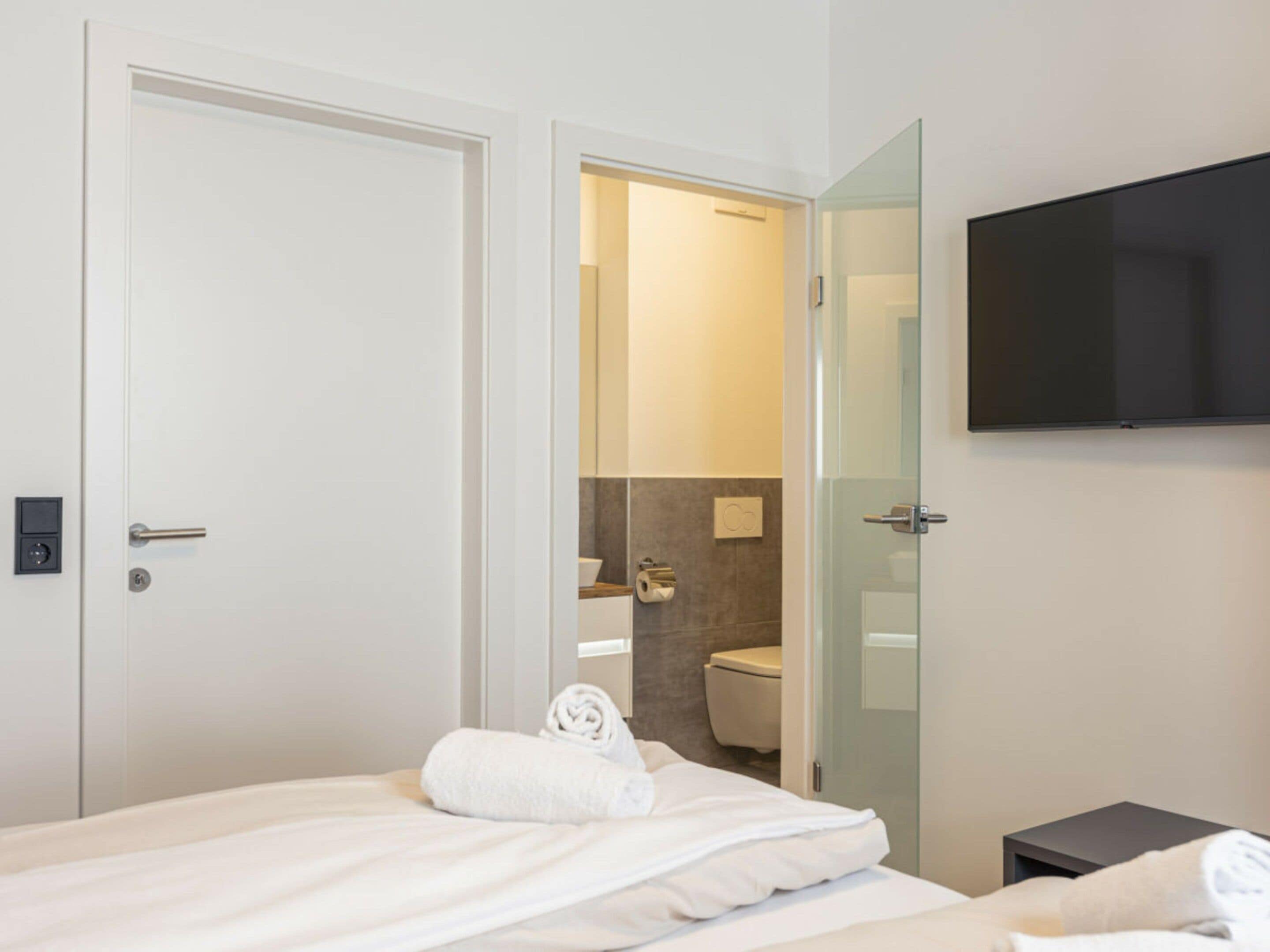 Une chambre d’hôtel avec un lit, un téléviseur fixé au mur et une salle de bain visible à travers une porte ouverte.