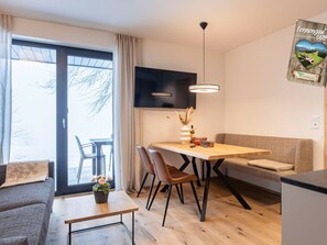 A modern living space with a dining area, a sofa, a TV, and a view through a large window. - Holiday Apartment & Infinity Pool (Sankt Martin am Tennengebirge)