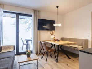A modern living space with a dining area, sofa, and a view through a glass door. - Holiday Apartment & Infinity Pool (Sankt Martin am Tennengebirge)