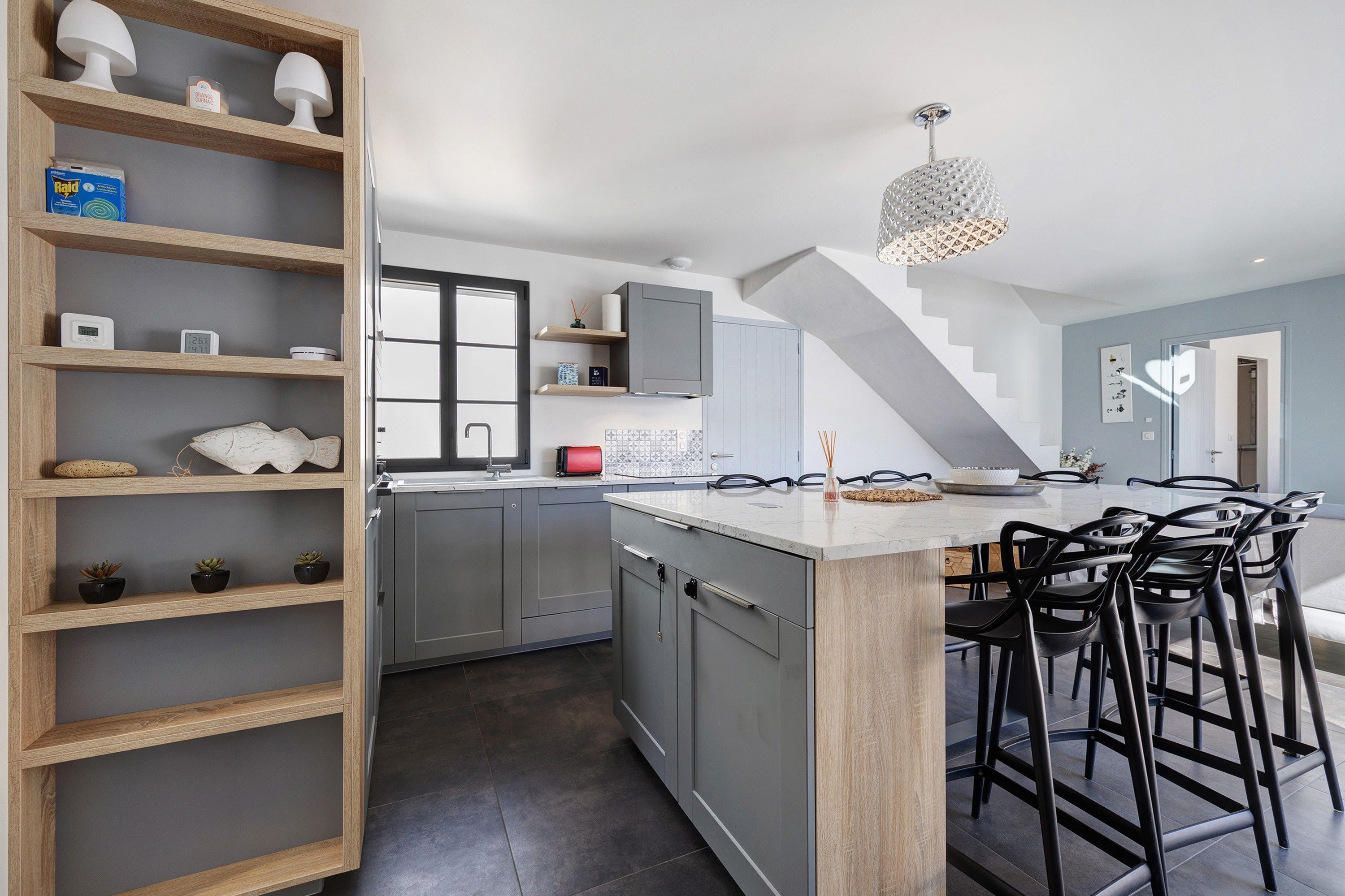 A modern kitchen with a central island, bar stools, and a staircase leading to another level.