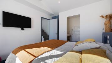 Un dormitorio con cama, televisor de pantalla plana montado en la pared, una escalera que sube a un nivel superior y una puerta que da al baño.