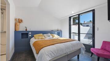 Ein modernes Schlafzimmer mit einem Bett, einem Sessel und Blick ins Freie.