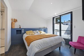Ein modernes Schlafzimmer mit einem Bett, einem Sessel und Blick ins Freie.