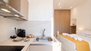 Una habitación de hotel compacta con kitchenette, una cama con manta amarilla y una mesita de noche con toallas.