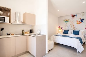 Una cucina moderna con microonde, piano cottura e lavello. C'è un letto con un murale floreale e un comodino con una lampada.