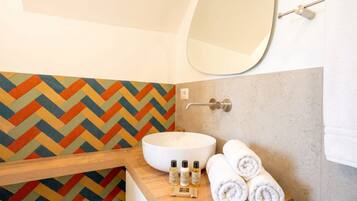 Une salle de bain avec un mur recouvert de carreaux disposés en motif chevrons, un lavabo blanc, un miroir et des serviettes soigneusement pliées.
