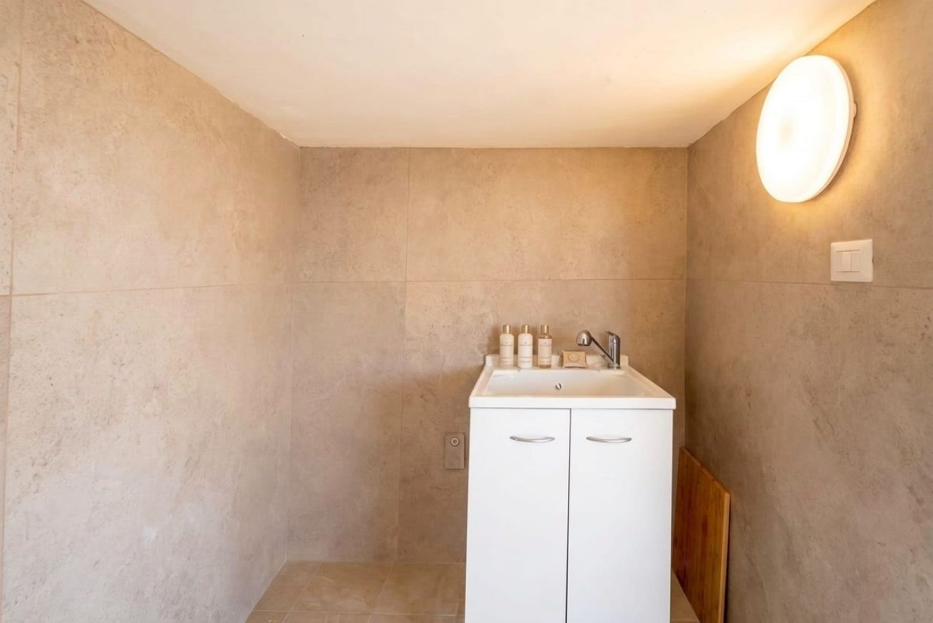 Une salle de bain avec un meuble blanc, un miroir et un luminaire fixé au mur.