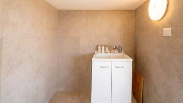 Une salle de bain avec un meuble blanc, un miroir et un luminaire fixé au mur.