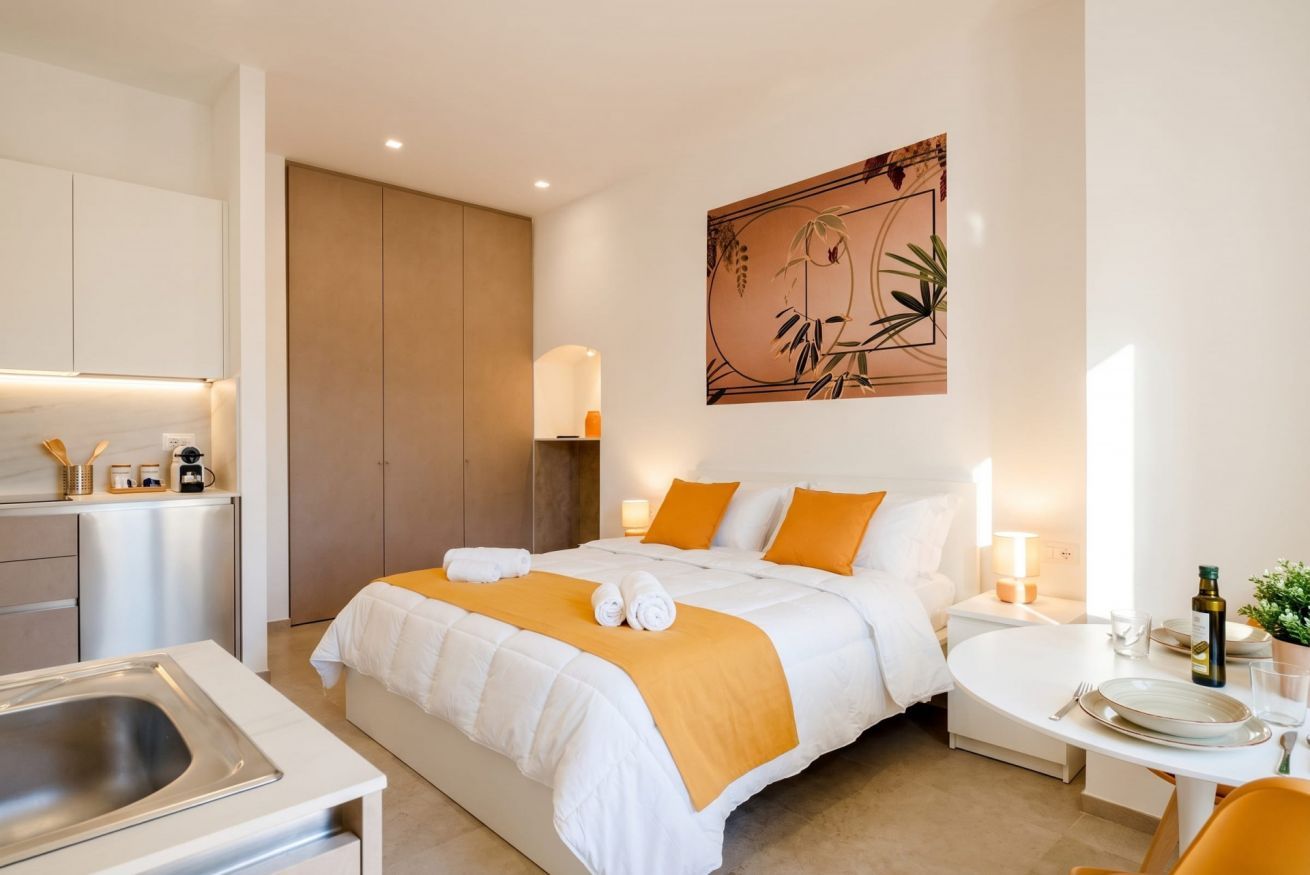 Habitación de hotel con cama, mesita de noche y zona de comedor.