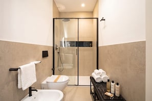 Un bagno moderno con doccia vetro, lavandino bianco e water. Asciugamani e articoli da toilette su uno scaffale.