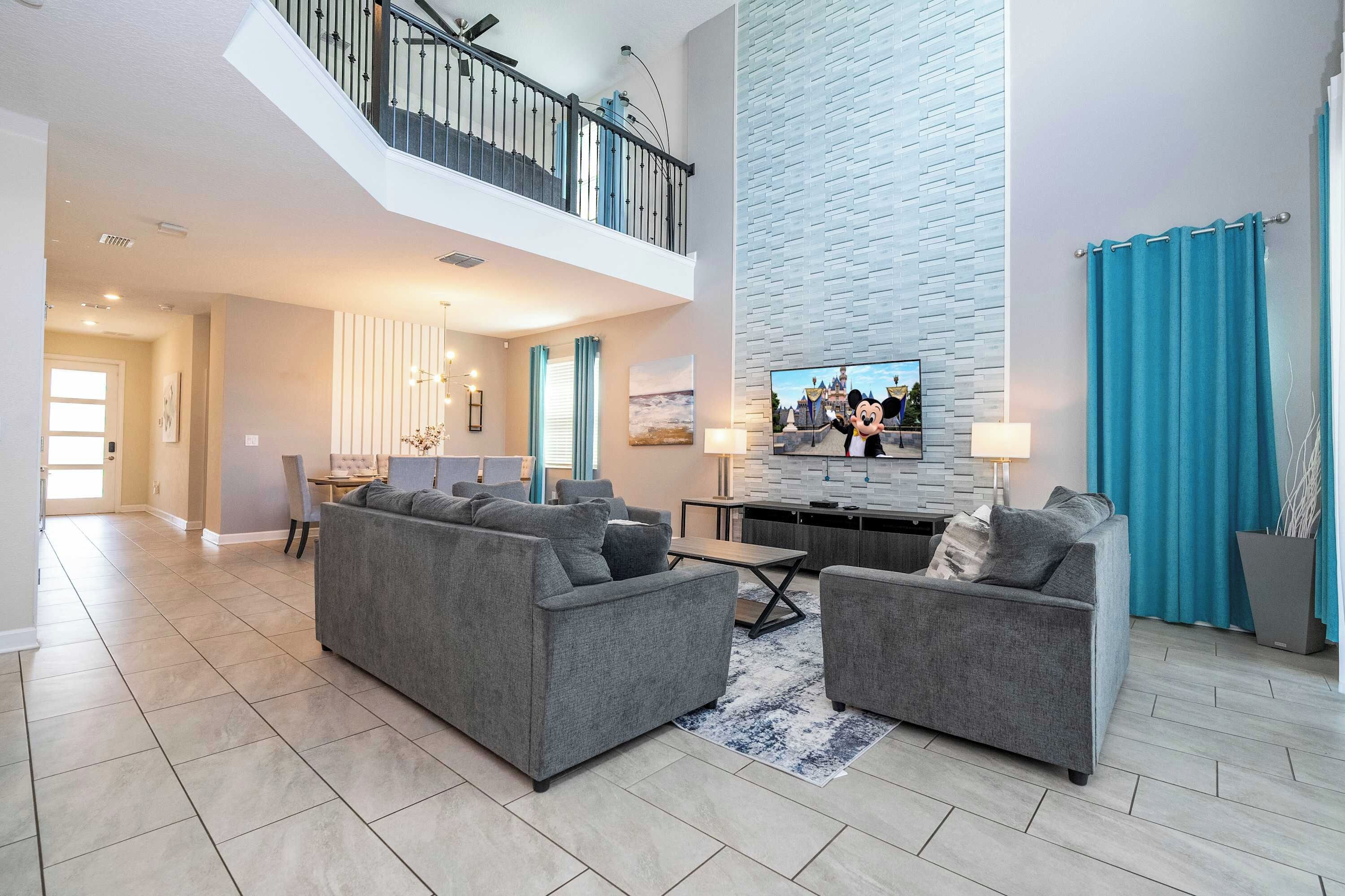 A spacious living area with a high ceiling, a staircase, a dining area, and a kitchen.