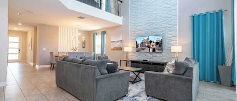 A spacious living area with a high ceiling, a staircase, a dining area, and a kitchen.