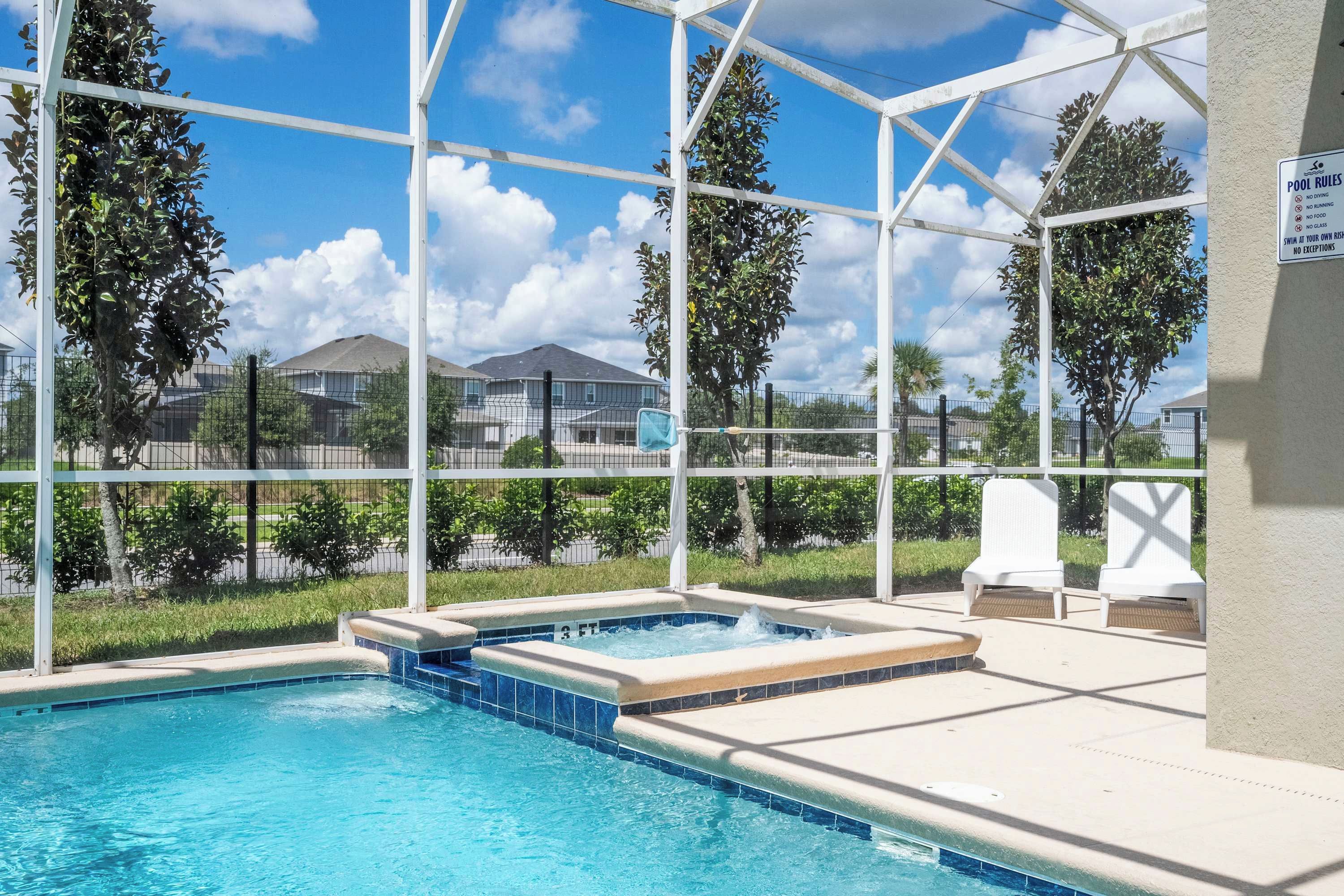 A pool area with a hot tub, lounge chairs, and a view of houses in the background.