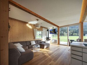 A spacious living room with a large sofa, a round coffee table, and a television mounted on the wall. - Cabin in Murau With Sauna and Terrace (Murau)