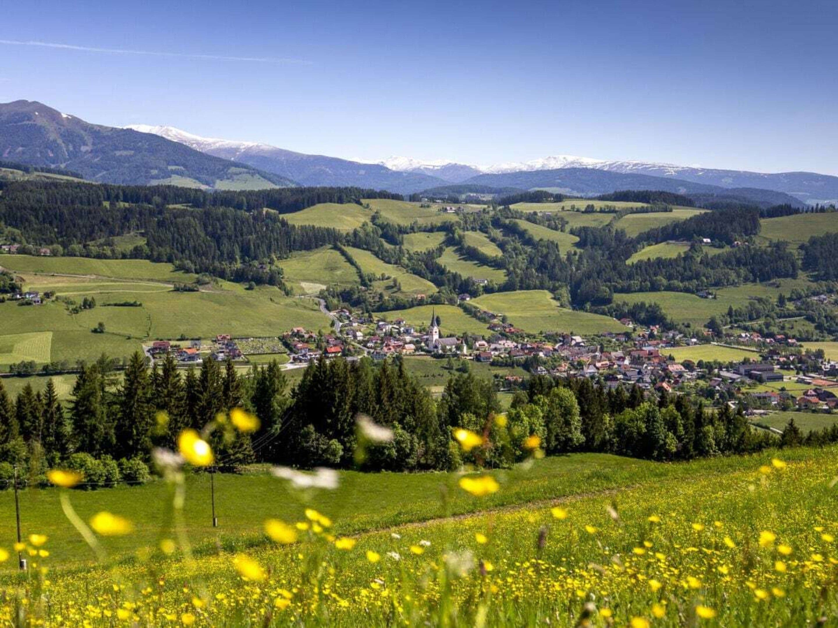 Ländliche Landschaft mit einem kleinen Dorf, sanften Hügeln und einem klaren Himmel.