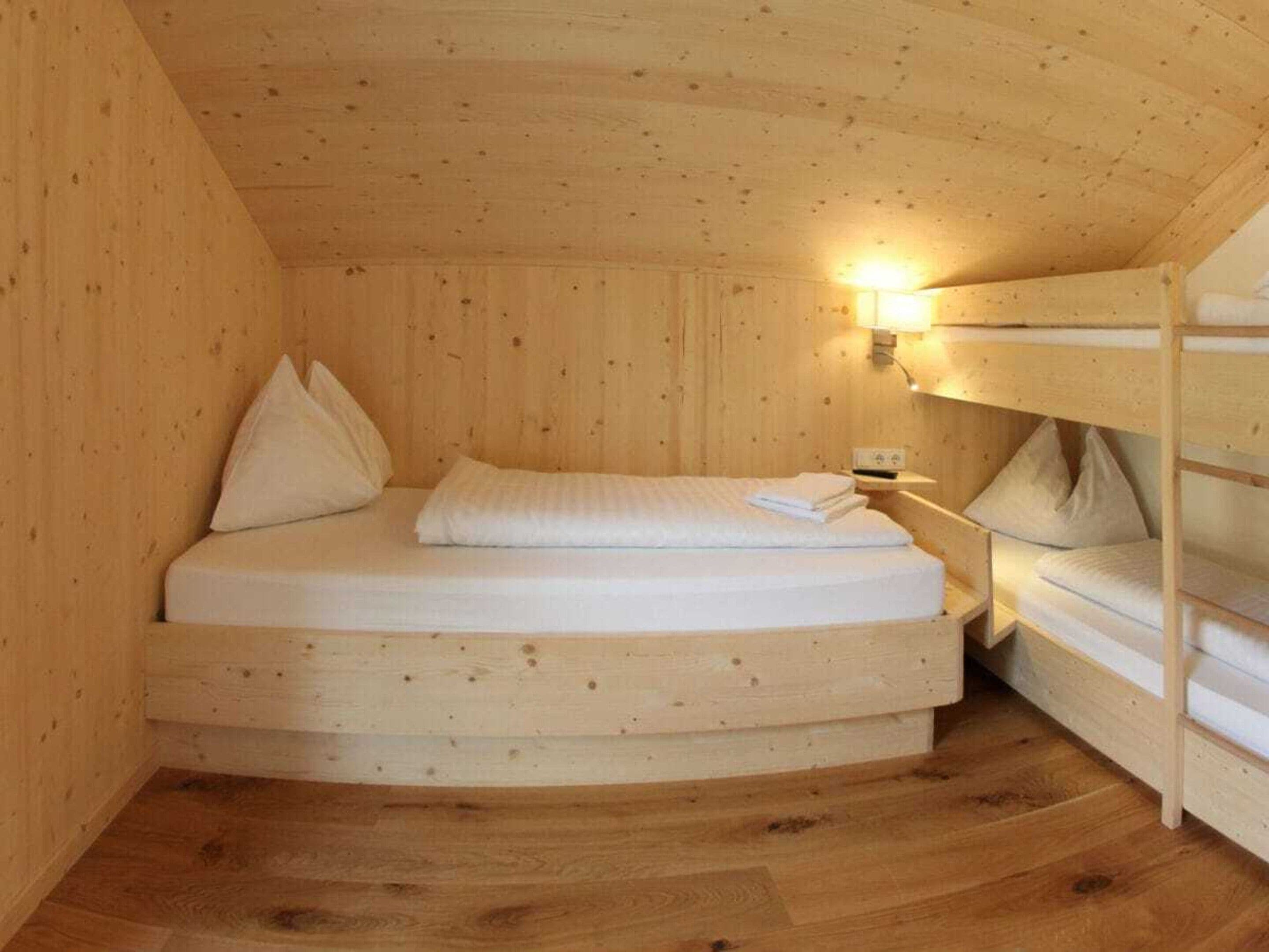 Une chambre dans un chalet en bois, équipée d’un lit superposé et d’un lit simple, tous deux avec du linge de lit blanc.