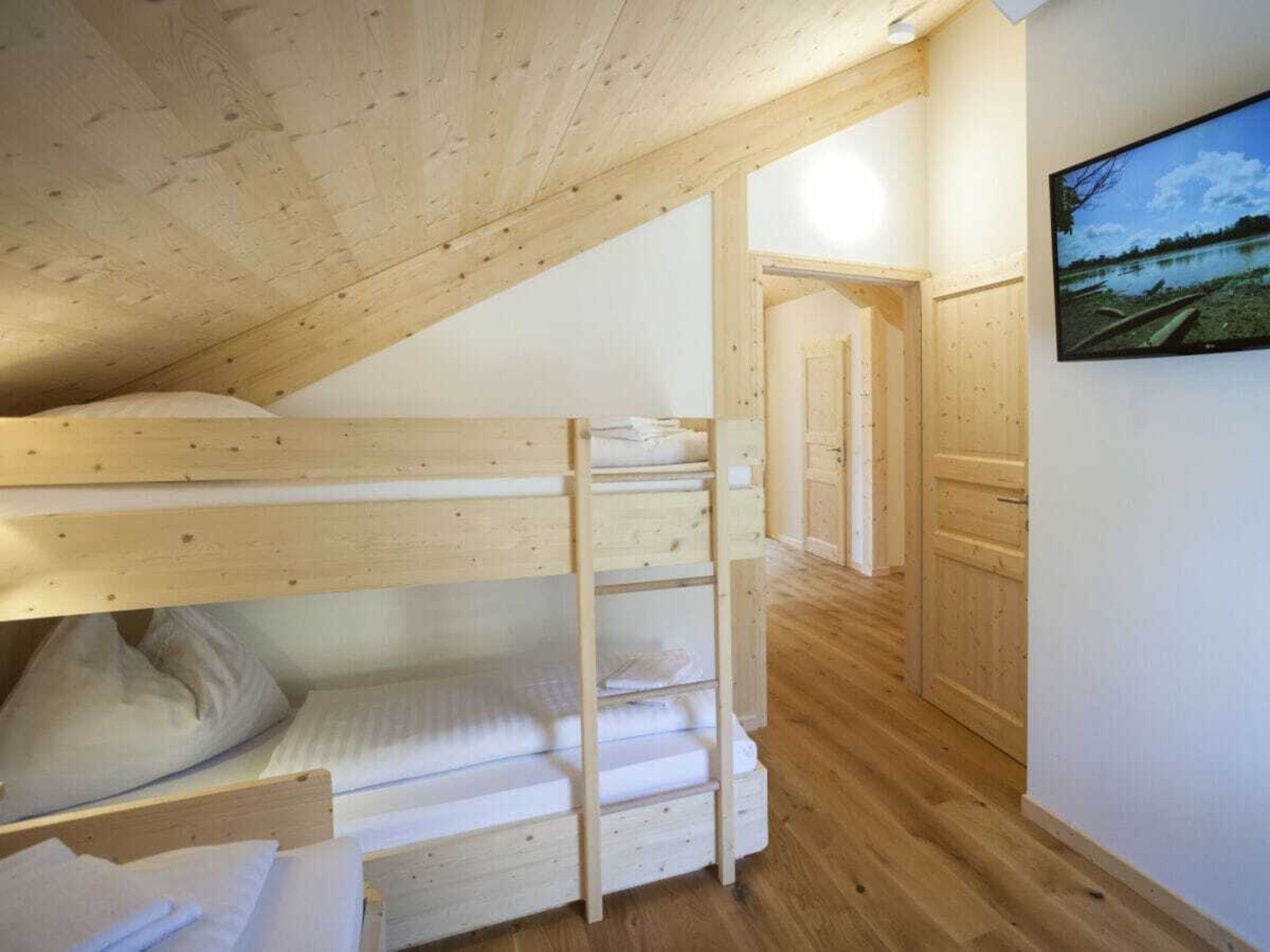 A bunk bed room with wooden beams, a ladder, and a painting on the wall.