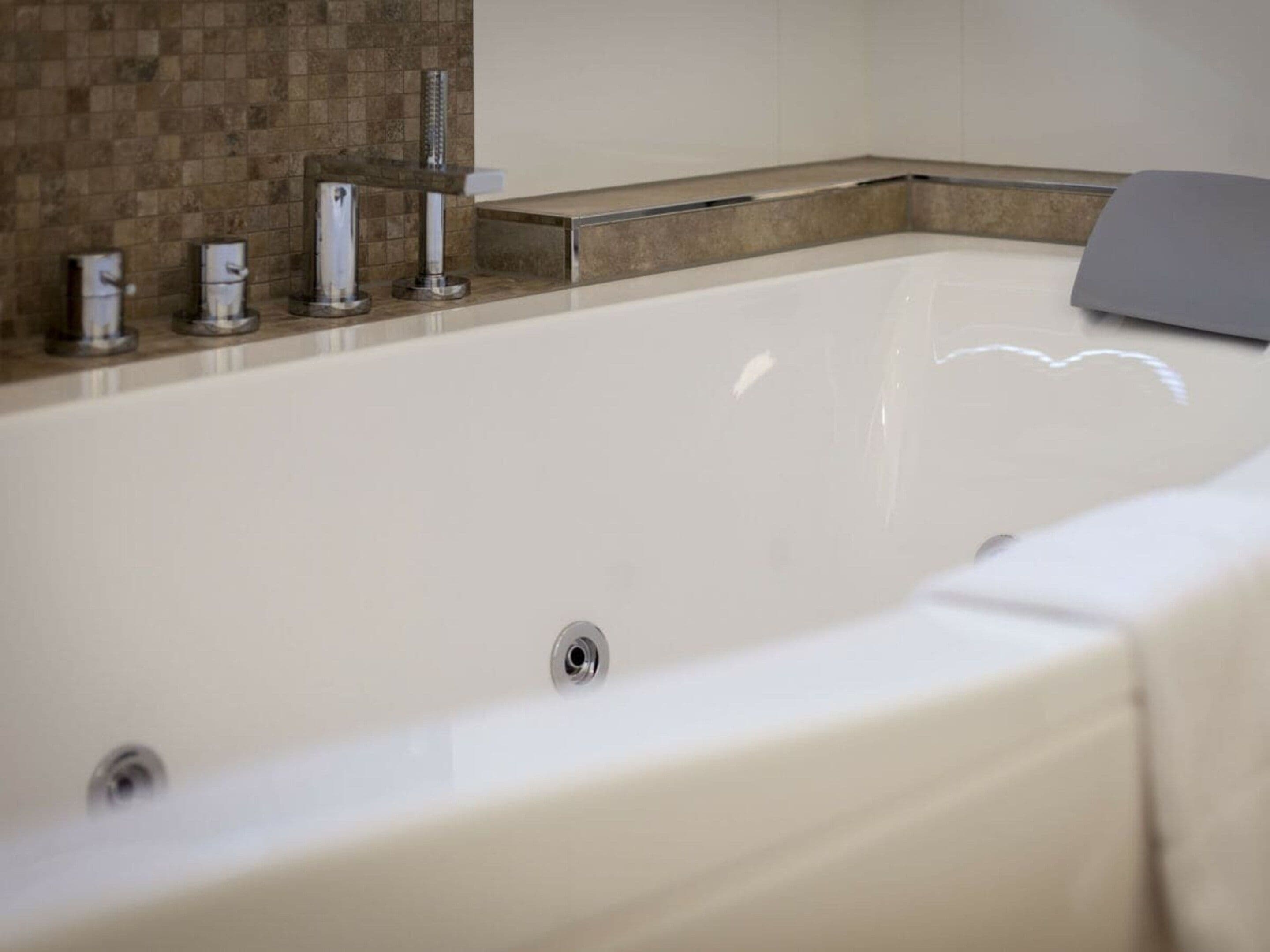 A large, rectangular bathtub with a chrome faucet and a drain.
