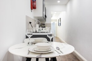 A narrow hallway with a dining table set for two, a white wall, and a kitchen area in the background. - Earl`s Court Residence | Elegant 1BR | London (London)