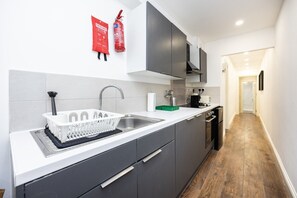 A modern kitchen with grey cabinets, a white countertop, a stainless steel sink, and a fire extinguisher mounted on the wall. - Earl`s Court Residence | Elegant 1BR | London (London)