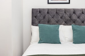 A bed with a tufted headboard, white bedding, and two teal pillows. - Earl`s Court Residence | Elegant 1BR | London (London)