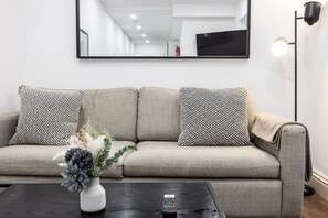 Ein sofa in neutraler Farbe, versehen mit gemusterten Kissen, eine Vase mit Blumen und eine Fernbedienung auf einem dunklen Couchtisch.